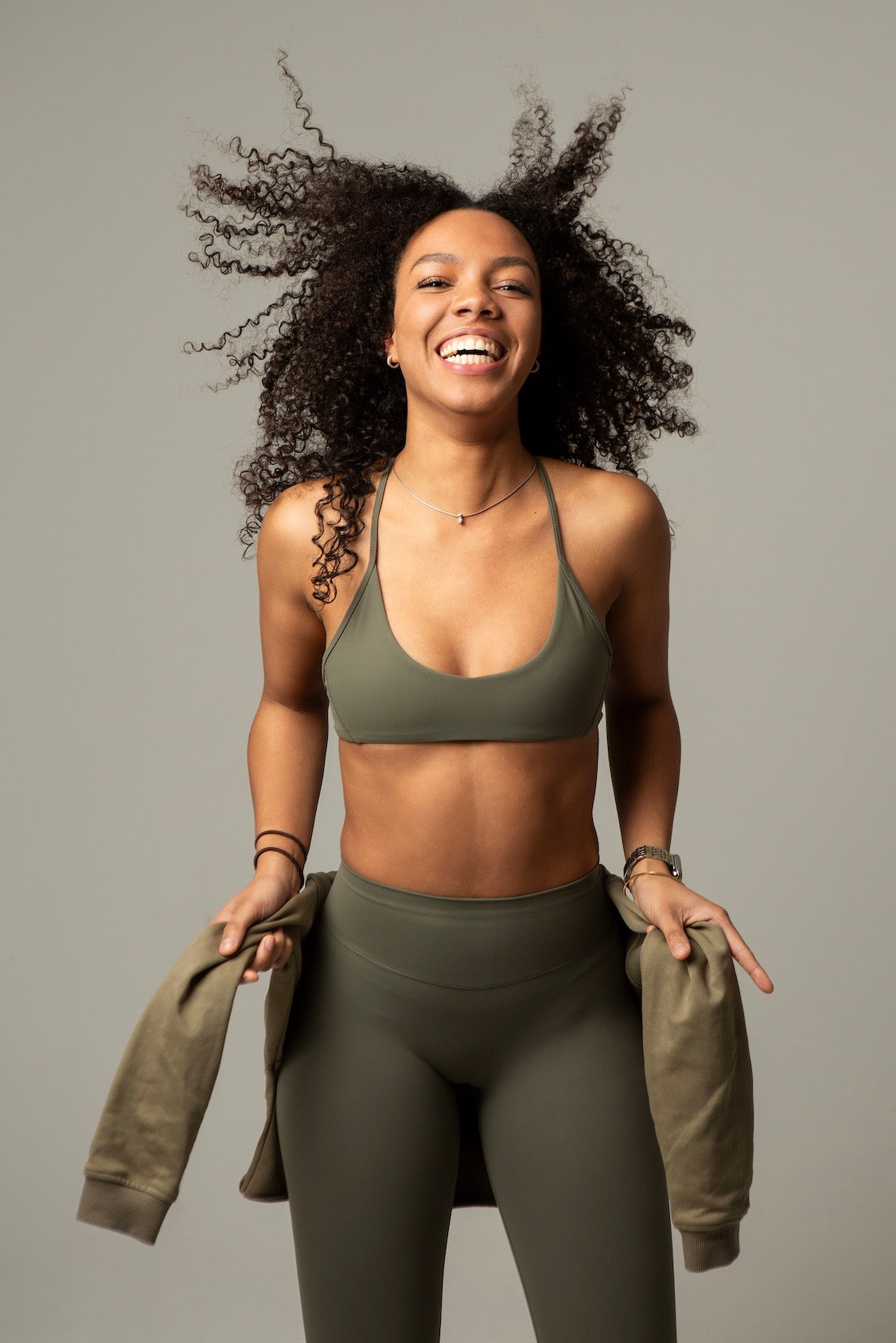 Model hebt Hoodie im aniri SculptAir Clean Bra in Khaki – sportlicher Look