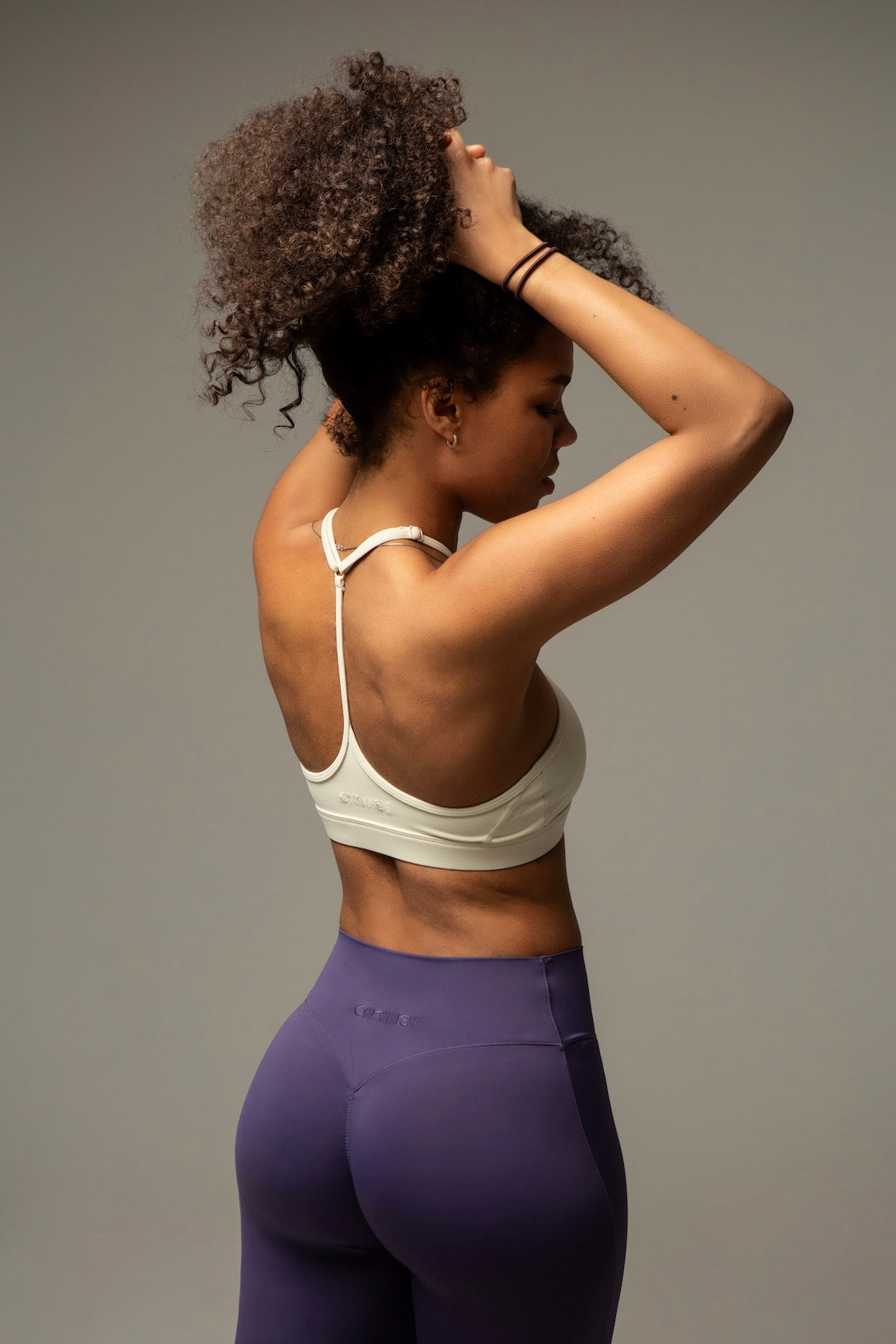 Rückenansicht Model im aniri SculptAir One-Shoulder Bra in Creme mit erhobenen Armen